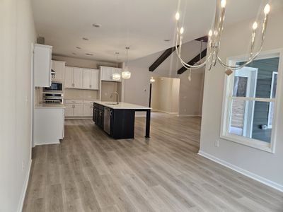 Bright, open kitchen with white cabinets, black island, pendant lights, and a spacious dining area with large windows.