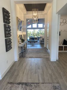 A stunning entryway with modern chandeliers, wood-look tile flooring, and an open layout leading to a bright living area.