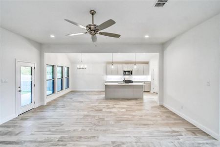 Kitchen featuring ceiling fan with notable chandelier, pendant lighting, a center island with sink, and light hardwood / wood-style floors