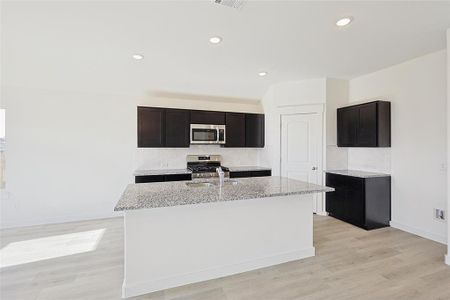 Kitchen featuring light stone counters, stainless steel appliances, sink, a center island with sink, and light hardwood / wood-style floors