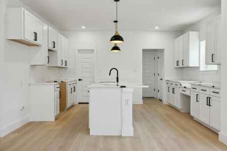 Kitchen with a kitchen island with sink, pendant lighting, white cabinetry, and light hardwood / wood-style floors