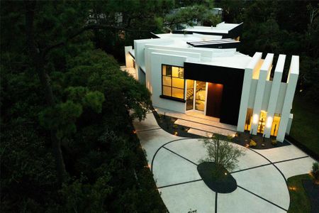 The circular driveway leads to an attached double dual-car bay showroom, offering space for a total of four cars. Landscape lighting accentuates the elegantly designed modern landscape, creating a stunning visual effect. The property itself spans just under one acre, providing both space and privacy in a lush, serene setting.