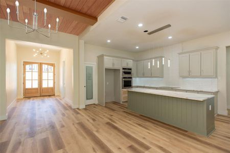 Kitchen featuring beamed ceiling, light hardwood / wood-style flooring, a kitchen island, an inviting chandelier, and hanging light fixtures