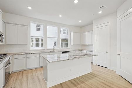 Kitchen with visible vents, backsplash, light wood-style flooring, stainless steel appliances, and a sink