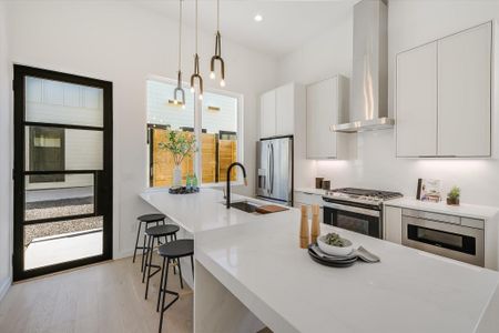 Kitchen with appliances with stainless steel finishes, pendant lighting, sink, white cabinets, and wall chimney exhaust hood