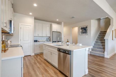 Kitchen with sink, appliances with stainless steel finishes, an island with sink, light hardwood / wood-style floors, and white cabinets