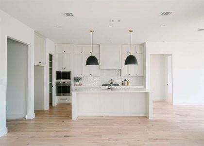 Kitchen with stainless steel appliances, light hardwood / wood-style floors, white cabinets, and a kitchen island with sink