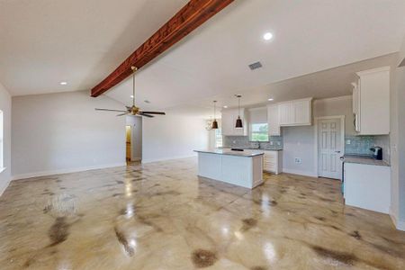 Kitchen featuring tasteful backsplash, lofted ceiling with beams, white cabinets, and a kitchen island