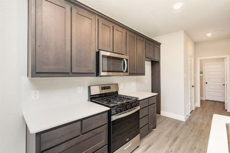 Kitchen featuring appliances with stainless steel finishes, dark brown cabinets, light wood-type flooring, and backsplash