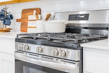 Room details featuring white cabinetry, decorative backsplash, and gas range