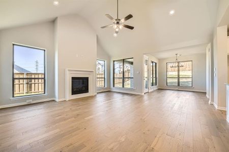 Unfurnished living room featuring ceiling fan with notable chandelier, light hardwood / wood-style floors, and high vaulted ceiling