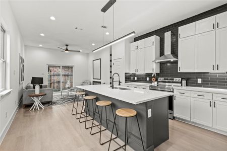 Kitchen featuring wall chimney range hood, white cabinetry, stainless steel electric range oven, and a kitchen island with sink