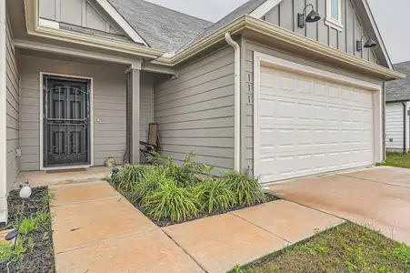 Property entrance with board and batten siding, a shingled roof, a garage, and concrete driveway Property entrance with board and batten siding, a shingled roof, a garage, and concrete driveway
