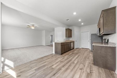 Kitchen featuring stainless steel appliances, ceiling fan, light carpet, and light stone counters