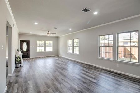 Unfurnished living room featuring dark wood-type flooring, ceiling fan, and ornamental molding