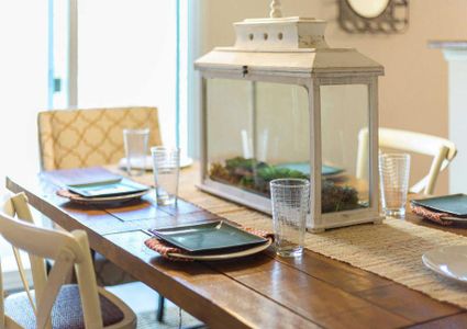 Staged dining room with wooden table and chairs, place settings with plates and glasses, and a white glass framed box centerpiece