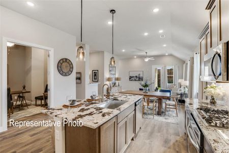 Kitchen featuring ceiling fan, hanging light fixtures, stainless steel appliances, an island with sink, and lofted ceiling