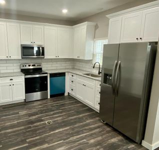 Kitchen featuring decorative backsplash, stainless steel appliances, white cabinets, dark wood-type flooring, and sink