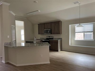 Kitchen with light hardwood / wood-style flooring, stainless steel appliances, sink, lofted ceiling, and light stone counters