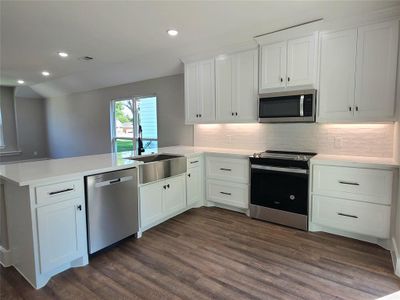 Kitchen with white cabinetry, dark wood-type flooring, backsplash, kitchen peninsula, and stainless steel appliances