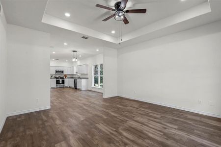 Unfurnished living room featuring sink, dark wood-type flooring, ceiling fan, and a raised ceiling