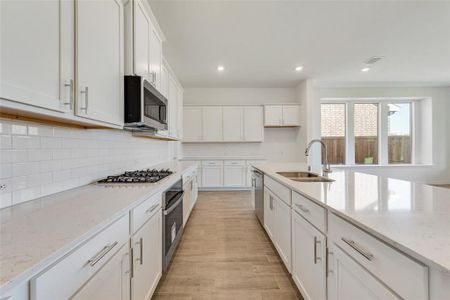 Kitchen featuring light stone countertops, backsplash, appliances with stainless steel finishes, sink, and white cabinets