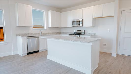 Kitchen with appliances with stainless steel finishes, sink, white cabinets, a center island, and light hardwood / wood-style floors