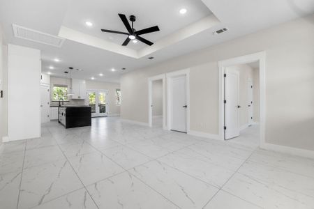 Unfurnished open and bright living room. featuring ceiling fan,  tray ceiling, and solid wood doors