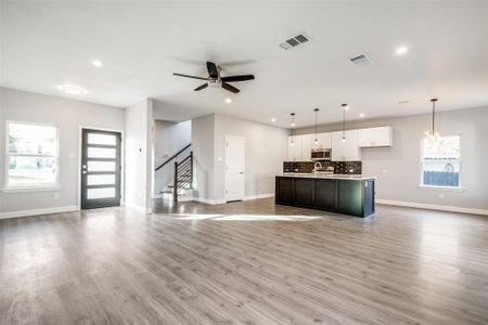 Kitchen with decorative light fixtures, white cabinets, decorative backsplash, a kitchen island with sink, and light wood-type flooring