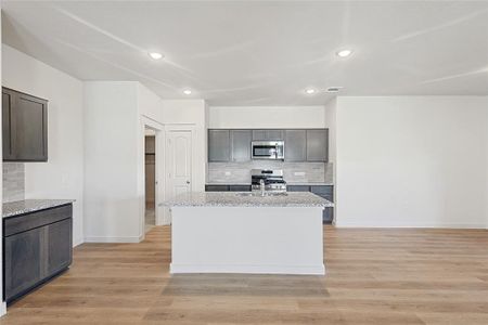 Kitchen featuring light stone countertops, a kitchen island with sink, stainless steel appliances, and light wood-type flooring