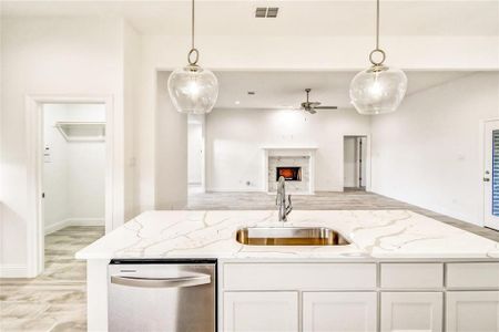 Kitchen with white cabinets, hanging light fixtures, dishwasher, sink, and a premium fireplace