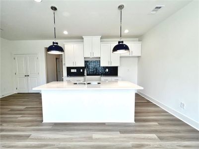 Kitchen with light hardwood / wood-style flooring, a kitchen island with sink, and decorative light fixtures