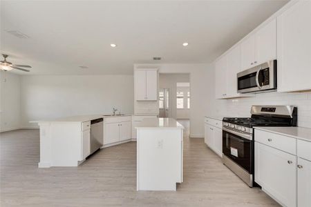 Kitchen featuring a kitchen island, light hardwood / wood-style flooring, decorative backsplash, white cabinets, and appliances with stainless steel finishes