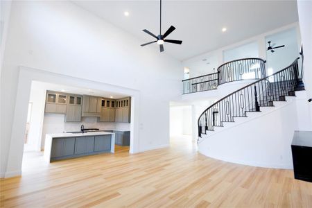 Unfurnished living room featuring sink, a towering ceiling, light hardwood / wood-style floors, and ceiling fan