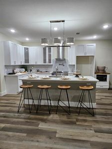 Kitchen featuring shaker white soft closing cabinets, a center island with sink, designer light fixtures, and stainless steel vent hood, pot filler, and 36" size stainless steel stove for gourmet chefs.