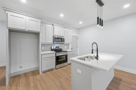 Kitchen with tasteful backsplash, stainless steel appliances, sink, pendant lighting, and an island with sink