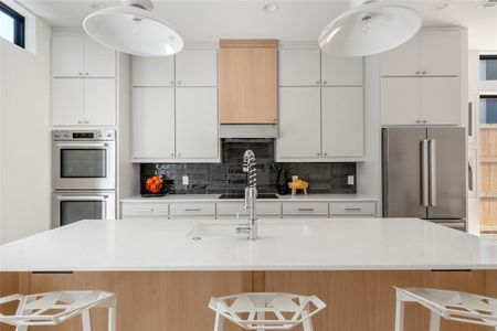 Kitchen with a kitchen breakfast bar, tasteful backsplash, an island with sink, stainless steel appliances, and white cabinetry