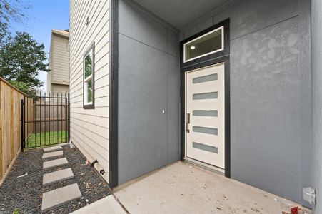 Modern entryway with a sleek front door featuring horizontal glass panels. The exterior blends light and dark tones, complemented by a narrow path with stepping stones leading to a fenced yard.