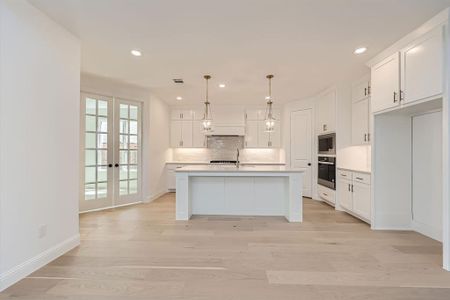 Kitchen with pendant lighting, a kitchen island with sink, white cabinets, light hardwood / wood-style flooring, and stainless steel appliances