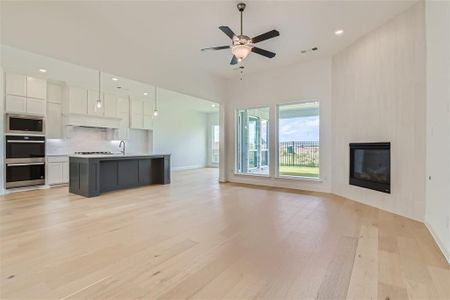 Unfurnished living room with light wood-type flooring, sink, a large fireplace, and ceiling fan