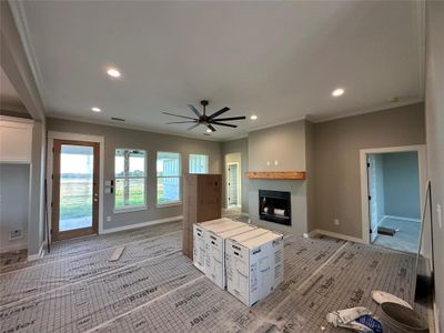 Unfurnished living room featuring a fireplace, light colored carpet, ceiling fan, and crown molding