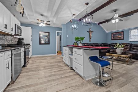 Kitchen featuring hanging light fixtures, appliances with stainless steel finishes, a kitchen breakfast bar, and white cabinetry