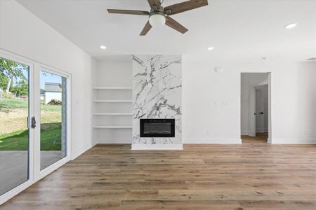 Unfurnished living room featuring a high end fireplace, ceiling fan, luxury vinyl flooring and built in features