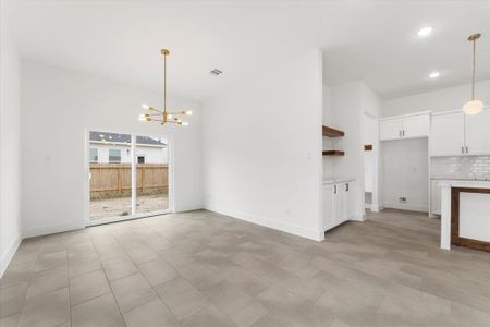 This dining space features a modern open-concept design with sleek tile flooring and crisp white walls. A stunning gold chandelier adds a touch of elegance, while the large sliding glass door fills the room with natural light and provides easy access to the backyard.