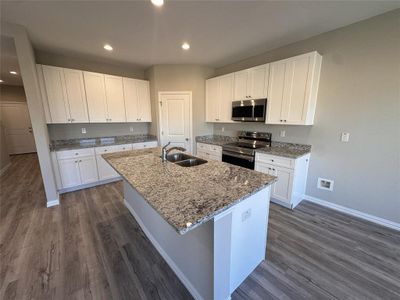 Kitchen featuring sink, white cabinetry, stainless steel appliances, and an island with sink