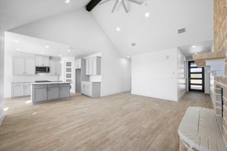 Unfurnished living room featuring light wood-type flooring, beam ceiling, a brick fireplace, and high vaulted ceiling