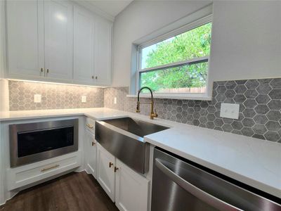 Kitchen with decorative backsplash, black microwave, stainless steel dishwasher, white cabinets, and dark wood-type flooring