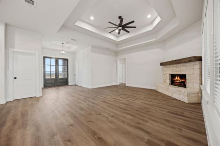 Unfurnished living room with baseboards, visible vents, wood finished floors, a tray ceiling, and a stone fireplace