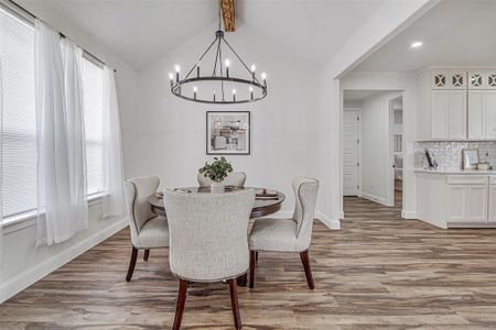 Dining space with vaulted ceiling with beams, light wood-type flooring, and an inviting chandelier