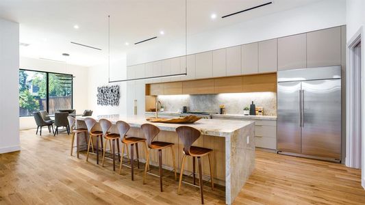 Kitchen featuring a large island with sink, stainless steel built in fridge, hanging light fixtures, and light wood-type flooring